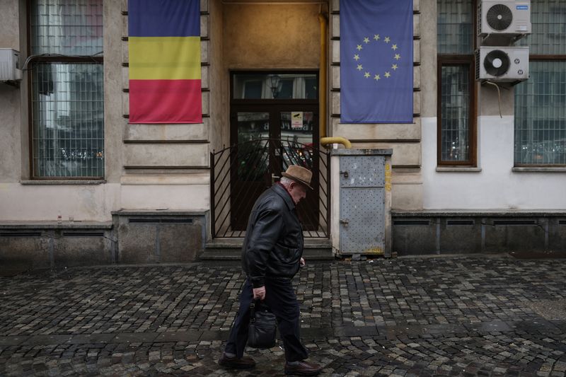 © Reuters. A man walks past a building with Romanian and EU flags in central Bucharest, following the annulment of the presidential election result, in Bucharest, Romania, December 7, 2024.  REUTERS/Louisa Gouliamaki