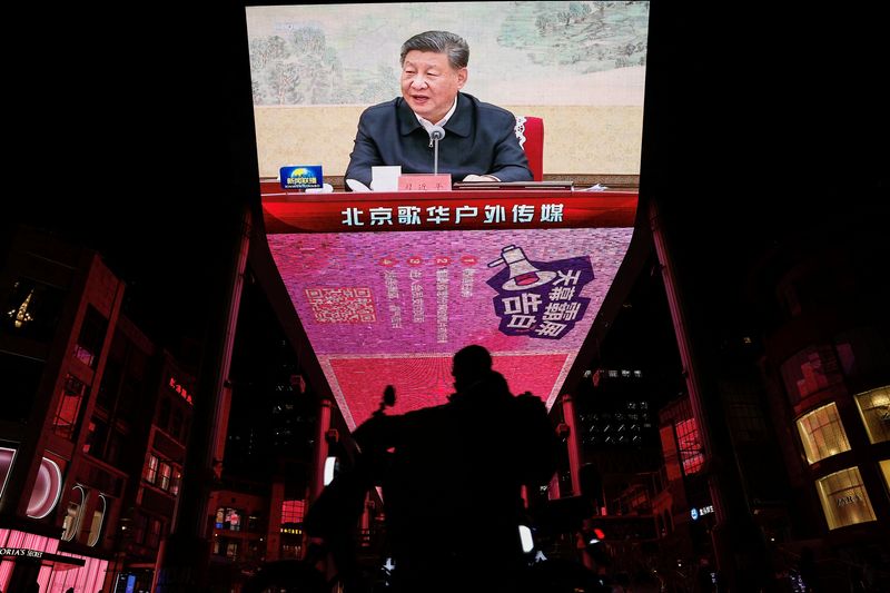 © Reuters. A man rides a scooter past a giant screen showing news footage of Chinese President Xi Jinping attending a Chinese Communist Party politburo meeting, in Beijing, China December 9, 2024. REUTERS/Tingshu Wang