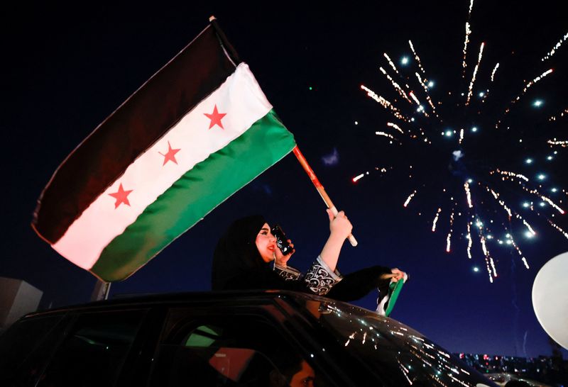 &copy; Reuters. A woman holds up the flag adopted by the new Syrian rulers, as people celebrate after fighters of the ruling Syrian body ousted Syria's Bashar al-Assad, in the Damascus old city, Syria, December 13, 2024. REUTERS/Ammar Awad  