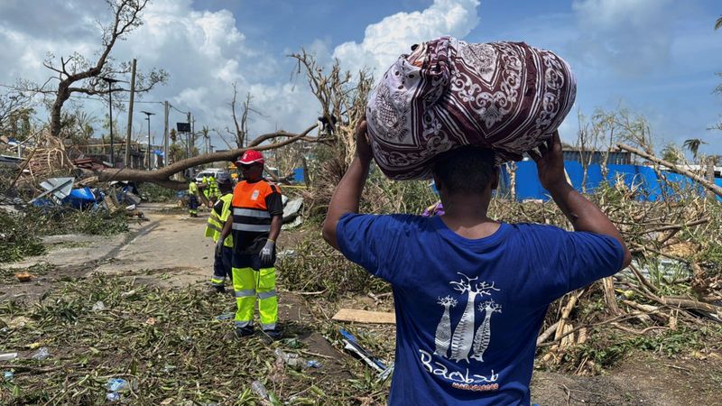 © Reuters. A man carries his belongings as rescue workers attempt to clear a blocked road, in the aftermath of Cyclone Chido, within Labattoir, in Mayotte, France, December 15, 2024. REUTERS/Chafion Madi