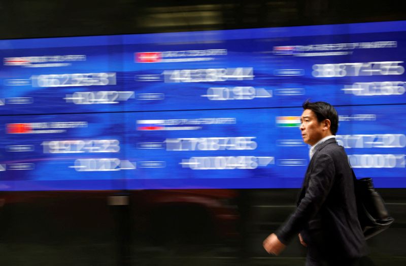 © Reuters. FILE PHOTO: A passerby walks past an electric monitor displaying the stock index of various countries in front of a bank in Tokyo, Japan March 22, 2023. REUTERS/Issei Kato/File Photo