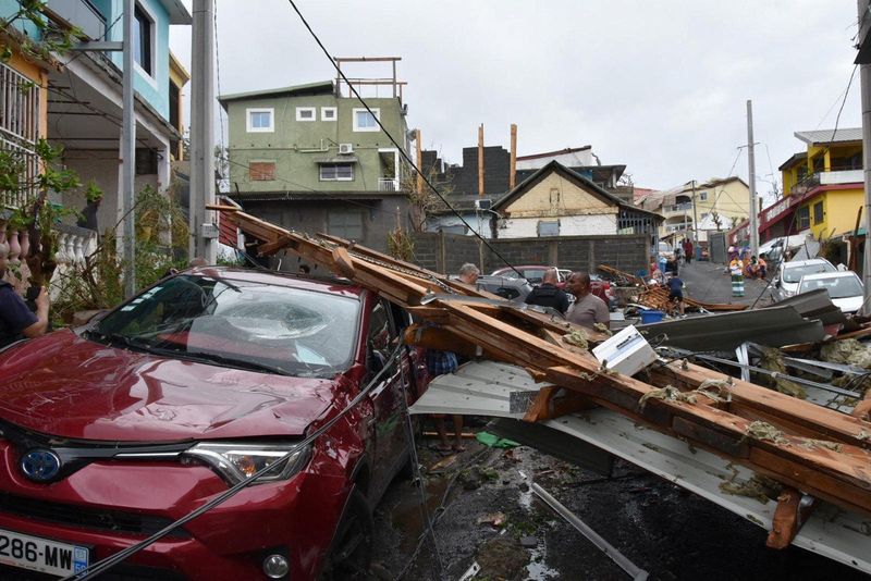 © Reuters. In this handout image obtained by Reuters on December 16, 2024, people stand near a damaged car covered in debris after Cyclone Chido in Mayotte, France. Ministere de l?Interior/Handout via REUTERS 