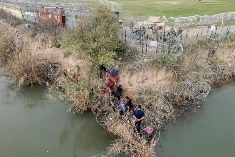 © Reuters. FILE PHOTO: A group of migrants attempt to go through a wire fence on the banks of the Rio Grande river as members of U.S. National Guards stand guard on the other side of the fence in Eagle Pass, Texas, U.S., February 27, 2024. REUTERS/Go Nakamura/File Photo