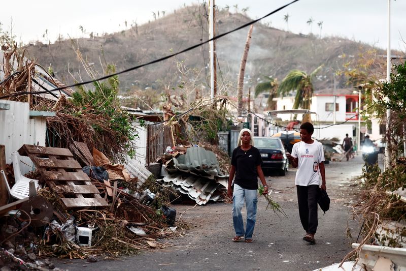 © Reuters. People walk on a street next to debris, in the aftermath of Cyclone Chido, in Pamandzi, Mayotte, France, December 17, 2024. REUTERS/Gonzalo Fuentes