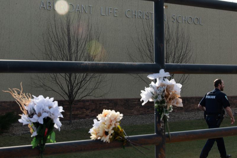 © Reuters. A police officer passes flowers left in memory of victims a day after a shooting at Abundant Life Christian School, in Madison, Wisconsin, U.S. December 17, 2024.  REUTERS/Cullen Granzen