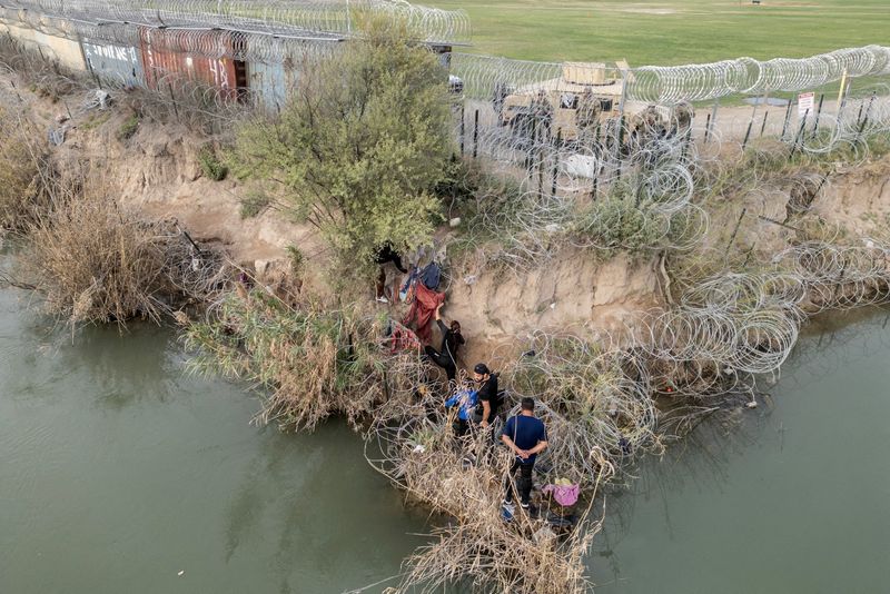 &copy; Reuters. FILE PHOTO: A group of migrants attempt to go through a wire fence on the banks of the Rio Grande river as members of U.S. National Guards stand guard on the other side of the fence in Eagle Pass, Texas, U.S., February 27, 2024. REUTERS/Go Nakamura/File P