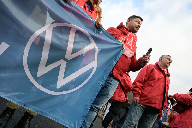 © Reuters. FILE PHOTO: A man wearing an IG Metall (Industrial Union of Metalworkers) scarf holds a banner with the Volkswagen logo, as workers gather to strike against planned cuts to wages and possible factory closures, in Hanover, Germany, December 2, 2024. Picture taken with long exposure. REUTERS/Fabian Bimmer/File Photo