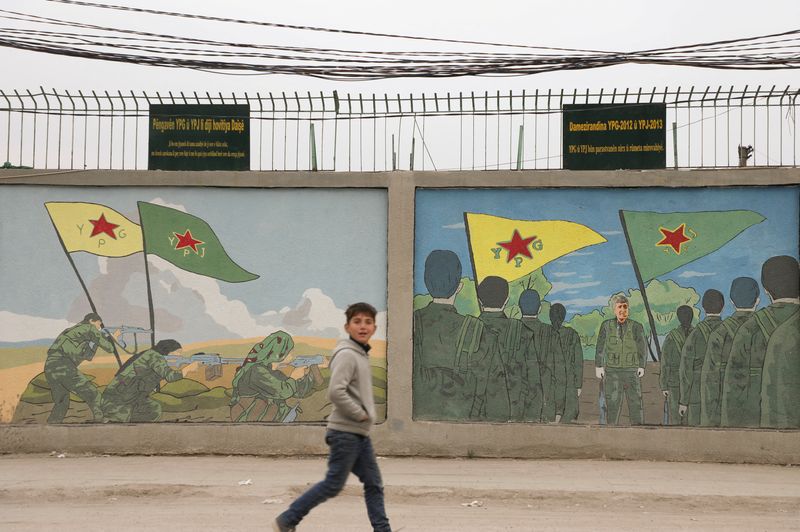 © Reuters. A boy walks past drawings on a wall showing flags of the Kurdish People's Protection Units (YPG) and the Women's Protection Unit (YPJ) in Qamishli, Syria, December 16, 2024. REUTERS/Orhan Qereman/Archive photo