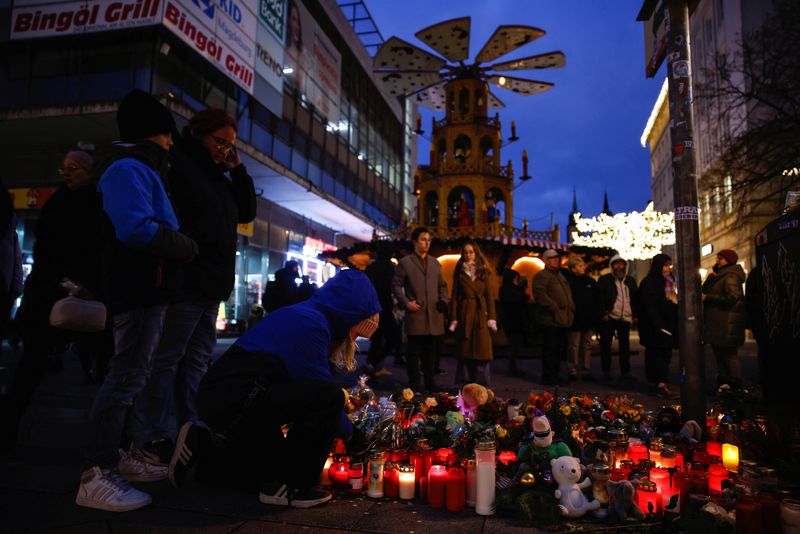 © Reuters. People look at flowers and candles left as a tribute for the victims of the 'Alter Markt' Christmas market, after a man drove a car into the crowd through an emergency exit route on Friday evening, in Magdeburg, Germany, December 23, 2024. REUTERS/Axel Schmidt