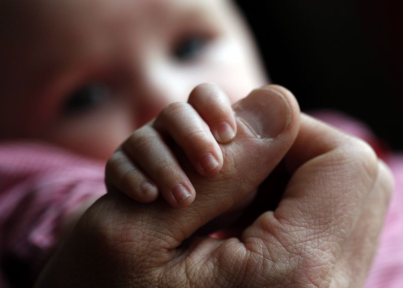 © Reuters. FILE PHOTO: A baby holds the hand of her father in this illustration. REUTERS/Michaela Rehle/File photo