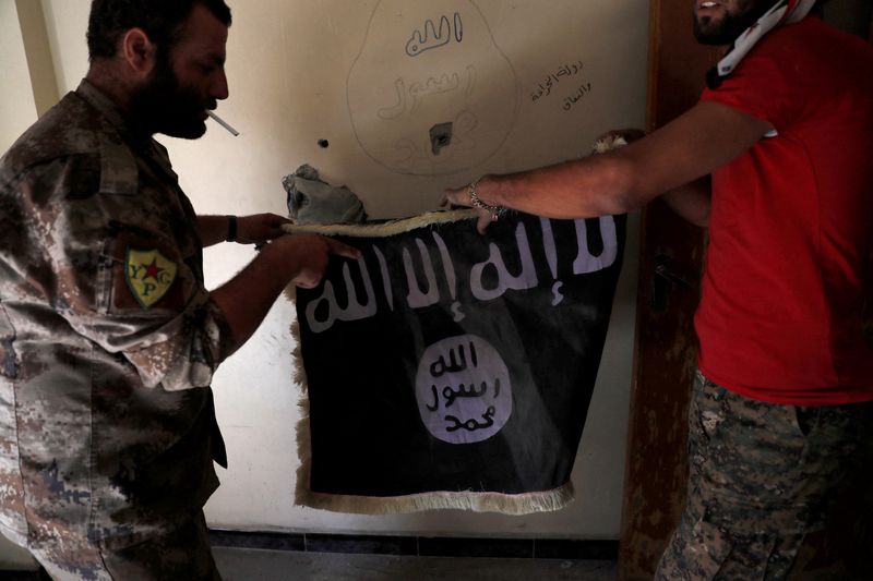 &copy; Reuters. FILE PHOTO: Members of Syrian Democratic Forces hold a flag of the Islamic State militants recovered at a building next to the stadium in Raqqa, Syria, October 4, 2017. REUTERS/Erik De Castro/File Photo