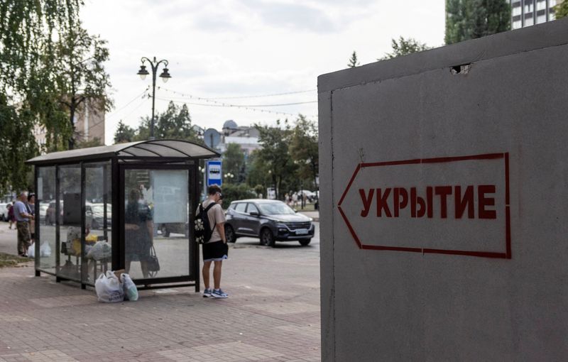 © Reuters. FILE PHOTO: People wait at a bus stop next to a reinforced concrete bomb shelter installed on a street during the conflict between Russia and Ukraine, in Kursk, Russia on August 28, 2024. The sign on the structure says: 