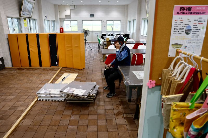 © Reuters. A man uses a phone as he pauses while cleaning the floor at a fish farm, where people can come and catch fish in artificial ponds and then cook and eat them at an adjoining restaurant, after the facility was flooded during Typhoon Shanshan in Yufu, Oita prefecture, southwestern Japan August 30, 2024.  REUTERS/Issei Kato/File Photo