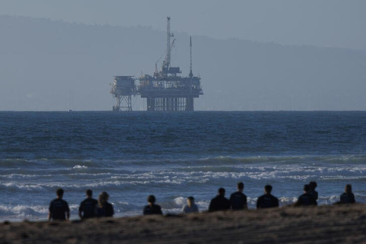 © Reuters. An offshore oil rig is seen as a group of people help clean the beach in Huntington Beach, California, U.S., November 14, 2024.  REUTERS/Mike Blake