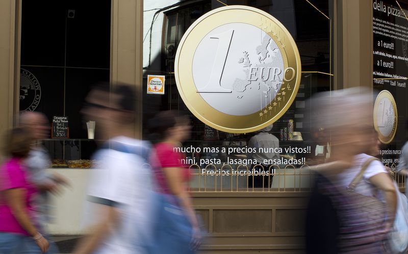 &copy; Reuters. FILE PHOTO: People walk past a pizza shop with a sign of a euro coin used to advertise its prices in central Madrid, September 13, 2011. REUTERS/Paul Hanna/File Photo