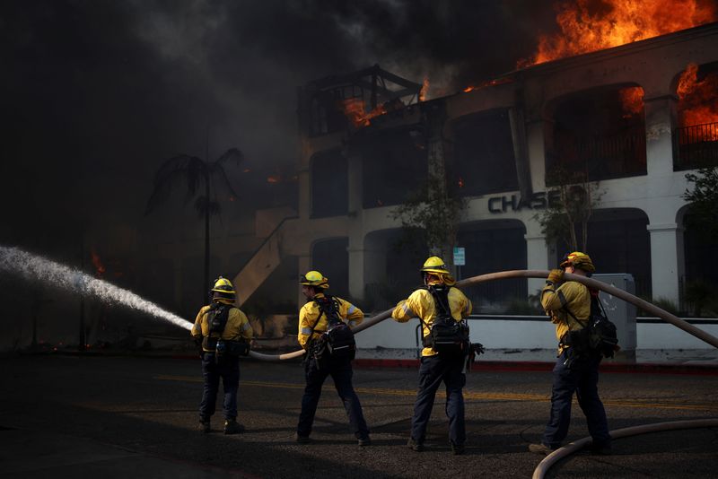 &copy; Reuters. Firefighter uses a hose near a burning building, as powerful winds fueling devastating wildfires in the Los Angeles area force people to evacuate, in the Pacific Palisades neighborhood on the west side of Los Angeles, California, U.S. January 8, 2025. REU