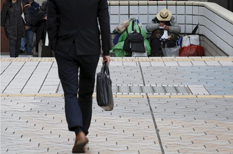 © Reuters. FILE PHOTO: A man (R) sits in a street as a businessman walks nearby at a business district in Tokyo, Japan, December 8, 2015. Picture taken December 8, 2015. REUTERS/Toru Hanai/File Photo