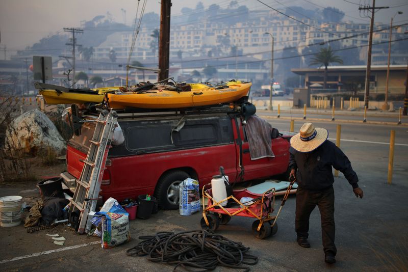 © Reuters. A man fetches water along the Pacific Coast Highway, as strong winds fueled wildfires in the Los Angeles area forcing people to evacuate, in the Pacific Palisades neighborhood west of Los Angeles, California, US January 8, 2025. REUTERS/Daniel Cole