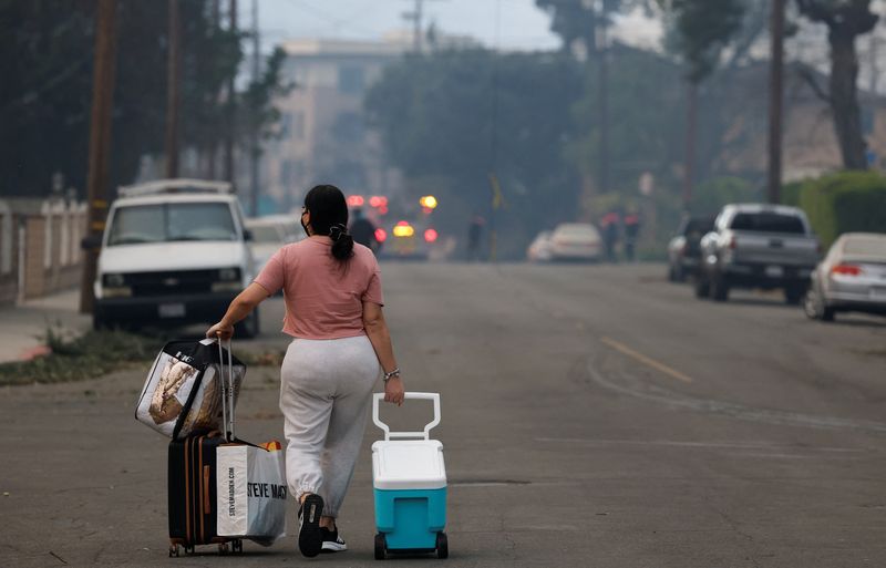 © Reuters. A woman with her belongings evacuates, as powerful winds fueling devastating wildfires in the Los Angeles area force people to evacuate, at the Eaton Fire in Altadena, California, U.S. January 8, 2025.  REUTERS/Fred Greaves