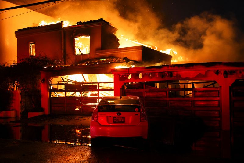 © Reuters. Smoke and flames rise from a burning home, as powerful winds fueling devastating wildfires in the Los Angeles area force people to evacuate, in Malibu, California, U.S. January 8, 2025. REUTERS/Daniel Cole