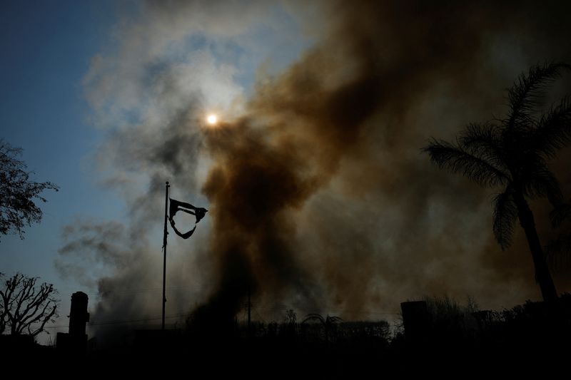 © Reuters. The remains of a U.S. flag flies as smoke rises from a burned house, as powerful winds fuel devastating wildfires, in the Pacific Palisades neighborhood in Los Angeles, California, U.S. January 9, 2025. REUTERS/Mike Blake   