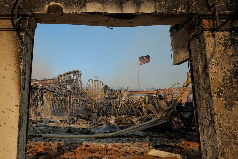 © Reuters. A U.S. flag flutters amid the remains of burnt buildings as powerful winds fueling devastating wildfires in the Los Angeles area force people to evacuate, in the Pacific Palisades neighborhood of west Los Angeles, California, U.S. January 8, 2025. REUTERS/Mike Blake