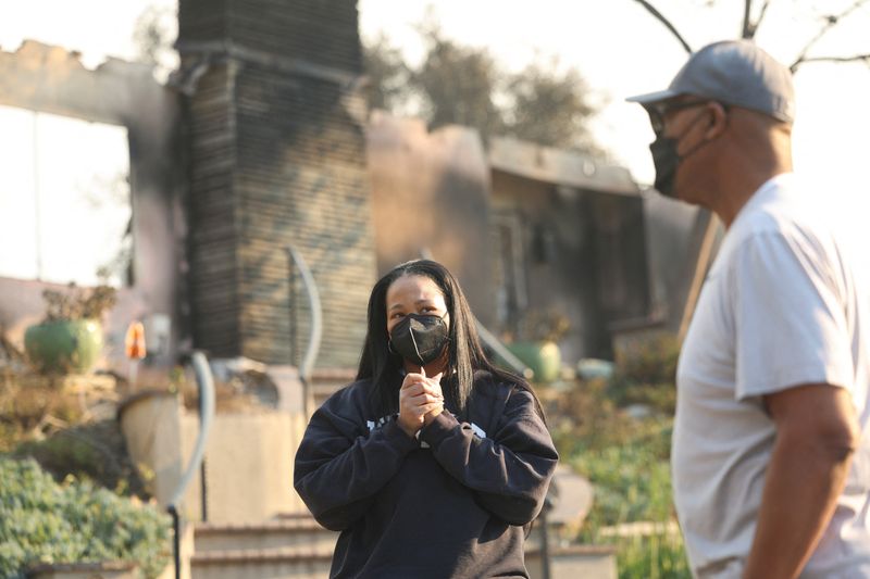 © Reuters. Inez Moore and her father Michael Moore stand near their burning family home after the Eaton Fire tore through a neighborhood, while a pair of massive wildfires threatening Los Angeles to the east and west still burn uncontained, in Altadena, California, US on January 9. 2025. Reuters/Mario Anzoni