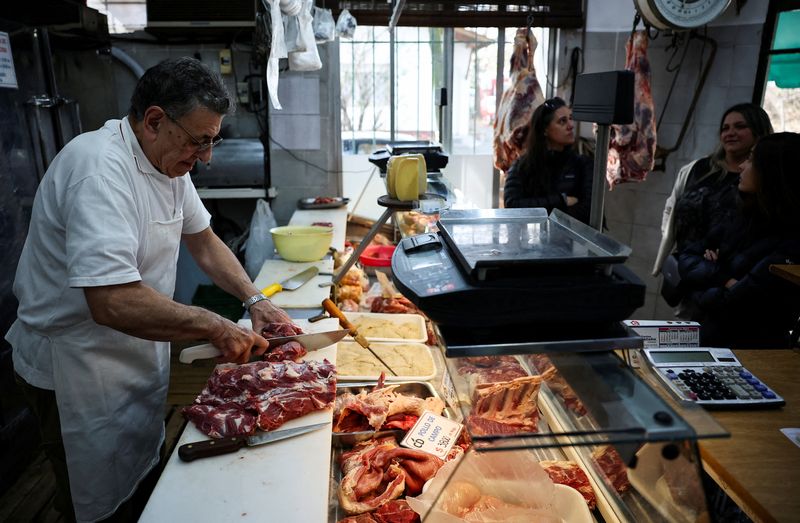 © Reuters. FILE PHOTO: Dario Barrandeguy chops meat in his butcher shop as customers wait, in Buenos Aires, Argentina June 10, 2024. REUTERS/Agustin Marcarian/File Photo