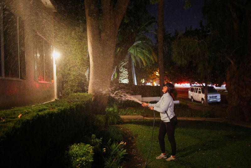 © Reuters. FILE PHOTO: A woman waters her front yard before leaving after an evacuation order, as wildfires burn in the Pacific Palisades area west of Los Angeles, Santa Monica, California, US, January 7, 2025. REUTERS/Daniel Cole/File Photo