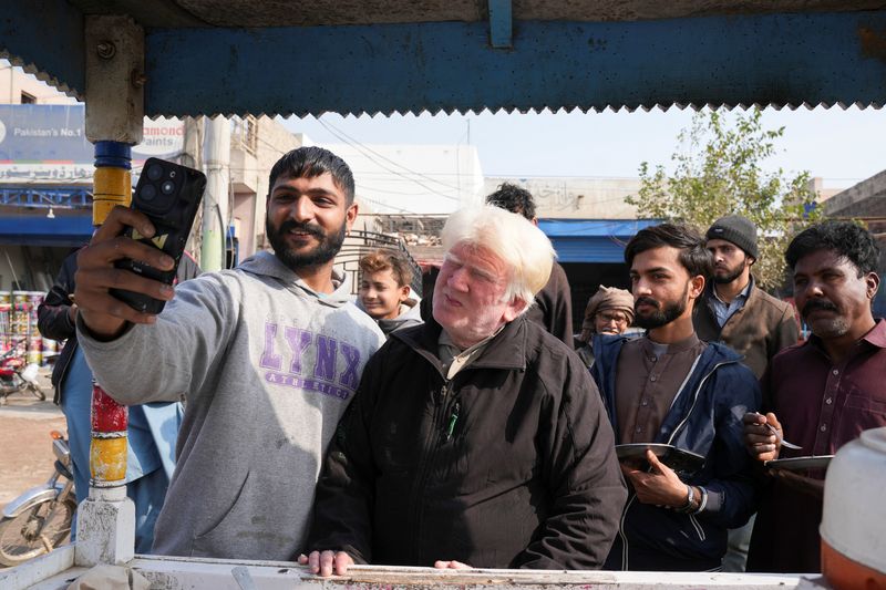 © Reuters. Salim Bagga, seen by some as a lookalike of US President-elect Donald Trump, takes a selfie with a customer while selling kheer, a traditional South Asian rice pudding, along a road in Sahiwal, Pakistan January 13, 2025. REUTERS/Nida Mebub