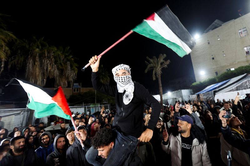 © Reuters. A man waves Palestinian flags as Palestinians react to news on a ceasefire deal with Israel, in Deir Al-Balah in the central Gaza Strip, January 15, 2025. REUTERS/Ramadan Abed