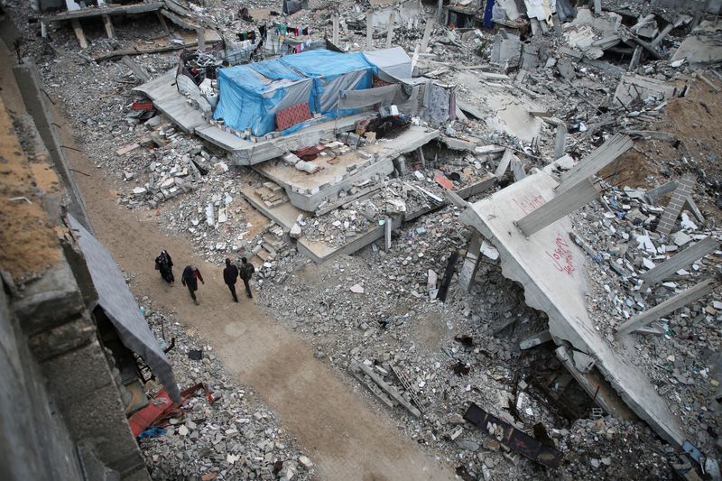 &copy; Reuters. Palestinians walk past the rubble of houses destroyed in previous Israeli strikes, ahead of a ceasefire set to take effect on Sunday, in Khan Younis in the southern Gaza Strip January 16, 2025. REUTERS/Hatem Khaled