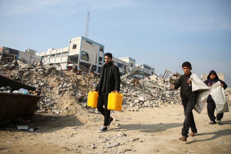 &copy; Reuters. Palestinians walk past the rubble of buildings destroyed in previous Israeli strikes, ahead of a ceasefire set to take effect on Sunday, in Khan Younis in the southern Gaza Strip January 16, 2025. REUTERS/Hatem Khaled