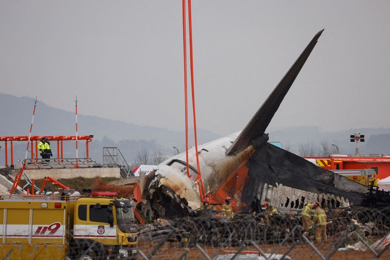 © Reuters. FILE PHOTO: People stand as a plane lies on the ground after it skidded off the runway and crashed at the Muan International Airport pictured in Muan, South Korea, December 30, 2024. REUTERS/Kim Soo- hyeon/File Photo