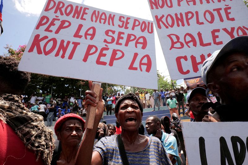 &copy; Reuters. FILE PHOTO: A woman holding a banner that reads in Haitian Creole “Drones are for the people, not against the people”, during a protest against insecurity, in Port-au-Prince, Haiti June 28, 2025. REUTERS/Jean Feguens Regala/File Photo