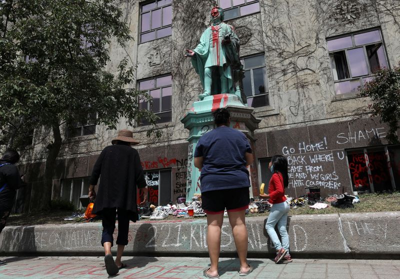 © Reuters. A First Nations family views the defaced Ryerson University statue of Egerton Ryerson, considered an architect of Canada's residential indigenous school system, following the discovery of the remains of 215 children on the site of British Columbia's former Kamloops Indian Residential School, in Toronto, Ontario, Canada June 2, 2021.  REUTERS/Chris Helgren