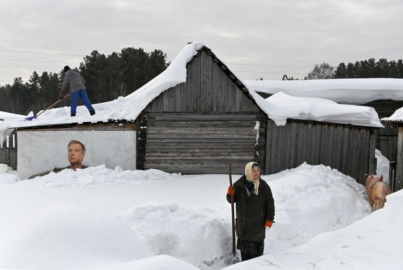 &copy; Reuters. A local resident removes snow from the roof of a wooden building above a banner with an image of Russian comedian Sergei Svetlakov in the village of Bobrovka in Omsk Region, Russia March 18, 2021. REUTERS/Alexey Malgavko