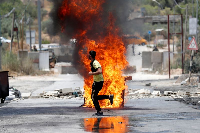 &copy; Reuters. متظاهر فلسطيني يمر بمتراس يحترق خلال اشتباكات مع القوات الإسرائيلية بالقرب من نابلس يوم الثلاثاء. تصوير: محمد تركمان - رويترز