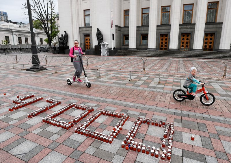 &copy; Reuters. A woman with a child ride near the candles commemorating 47000 victims of the coronavirus disease (COVID-19) during a protest demanding the resignation of Ukrainian Health Minister Maksym Stepanov in front of the parliament building in Kyiv, Ukraine May 1