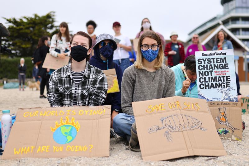 &copy; Reuters. Two people sit with signs during a protest of Cornwall Climate Youth Alliance in partnership with Fridays for Future and Climate Live, at Gyllyngvase Beach, in Falmouth, on the sidelines of G7 summit in Cornwall, Britain, June 11, 2021. REUTERS/Tom Nichol