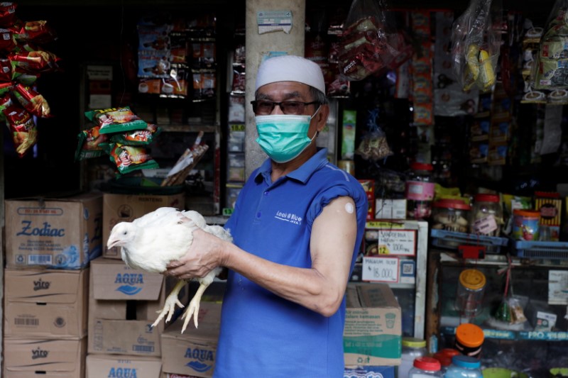 &copy; Reuters. رجل يمسك دجاجة حية حصل عليها كجائزة بعد تلقيه الجرعة الأولى من اللقاح الواقي من فيروس كورونا في قرية بجاوة الغربية يوم الثلاثاء. تصوير: ويلي 