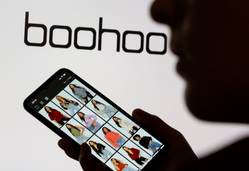 &copy; Reuters. FILE PHOTO: A woman poses with a smartphone showing the Boohoo app in front of the Boohoo logo on display in this illustration taken September 30, 2020. REUTERS/Dado Ruvic/Illustration/File Photo