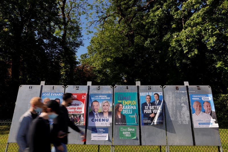 © Reuters. FILE PHOTO: People, wearing a protective face mask, walk past electoral panels ahead of the upcoming French regional elections in Cambrai, France, June 1, 2021. REUTERS/Pascal Rossignol