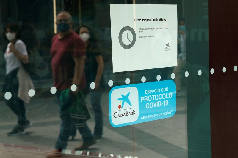&copy; Reuters. People walk past a Caixabank's branch displaying a sign that reads "Office branch closed temporarily. This office will be closed throughout the day"  during a one-day strike called by unions against the bank's plans for layoffs in Madrid, Spain, June 22, 