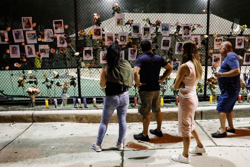 &copy; Reuters. أشخاص ينظرون إلى زهور وصور لمفقودين على سياج عند نصب تذكاري لضحايا انهيار مبنى سكني بينما تواصل فرق الطوارئ عمليات البحث والإنقاذ عن ناجين 