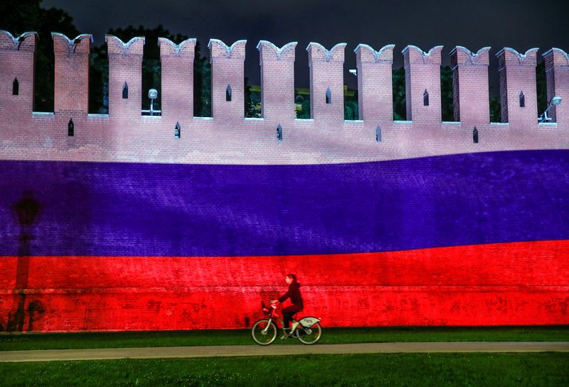 &copy; Reuters. Una donna va in bicicletta lungo il muro del Cremlino, su cui è proiettata una banidera russa. Mosca, Russia, 12 giugno 2020 REUTERS/Maxim Shemetov