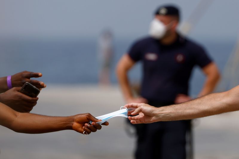 &copy; Reuters. Un Carabiniere offre una mascherina ad un migrante in procinto di salire su un traghetto in uscita da Lampedusa. 22 giugno 2021 REUTERS/Guglielmo Mangiapane/File Photo