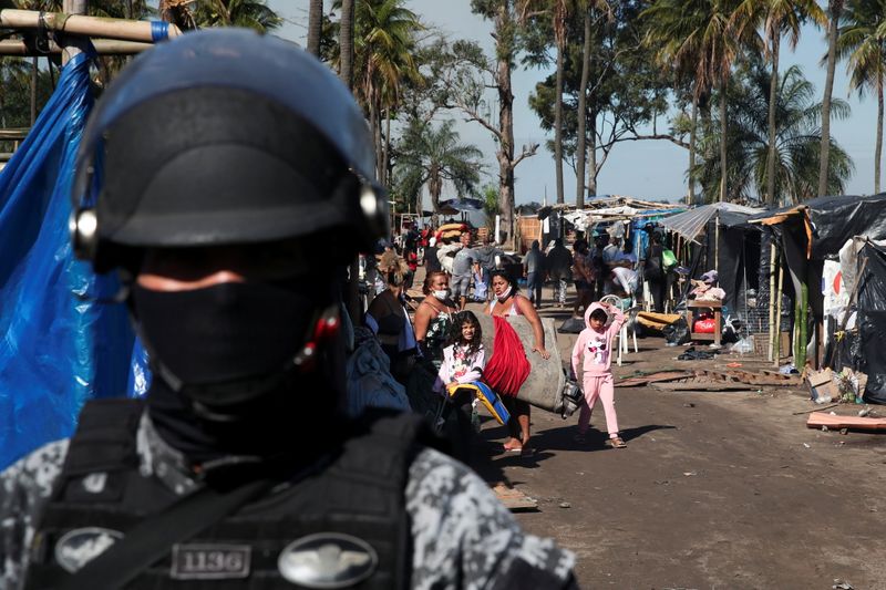 © Reuters. Pessoas carregam seus pertences observadas por policial do batalhão de choque durante reintegração de posse em Itaguaí
01/07/2021 REUTERS/Ricardo Moraes