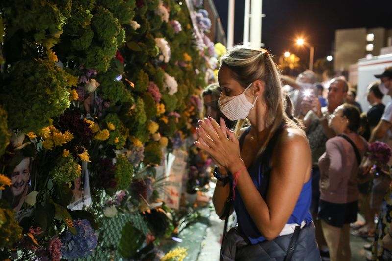 © Reuters. FILE PHOTO: A woman prays as people mourn at the memorial site created by neighbors in front of the partially collapsed building where the rescue personnel continue their search for victims, in Surfside near Miami Beach, Florida, U.S. June 28, 2021. REUTERS/Marco Bello