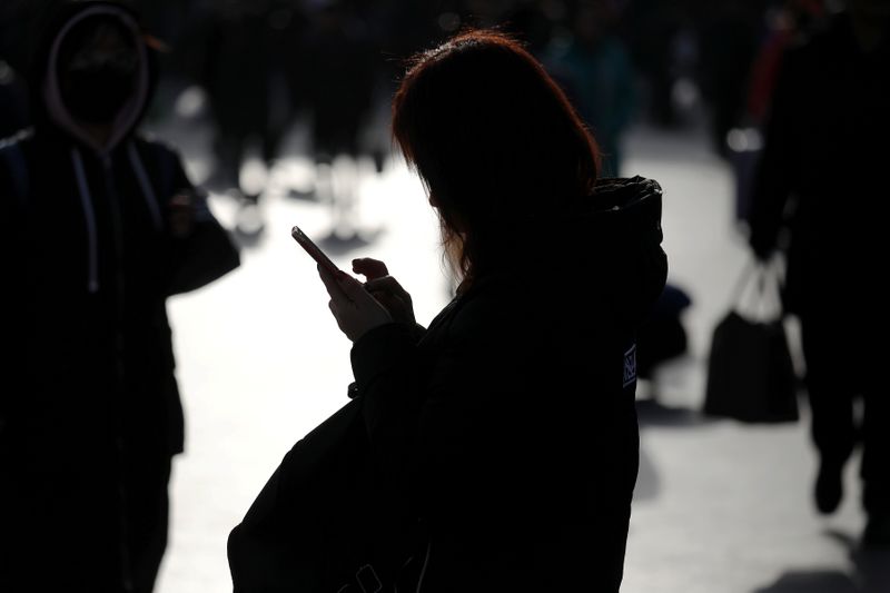 &copy; Reuters. FILE PHOTO: A woman checks her phone as passengers arrive at the Beijing Railway Station in central Beijing, China February 1, 2018. REUTERS/Damir Sagolj/File Photo